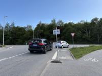 Udkørsel fra Tonne kjærsvej. Der kan være meget trafik i myldretiden. Cyklister som skal svinge til venstre kommer i konflikt med biler som svinger til højre. Rampen til cykelstien på modsatte side befinder sig i lige linje gennem den grå bil. 